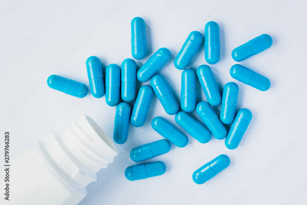 Blue capsules, pills on a light blue background. Capsules in a white jar. Vitamins, nutritional supplements for women's health Blue capsules, pills on a light blue background. Capsules in a white jar. Vitamins, nutritional supplements for women's health
