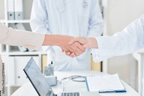 Doctor shaking hand of female patient over office table with opened laptop  selective focus