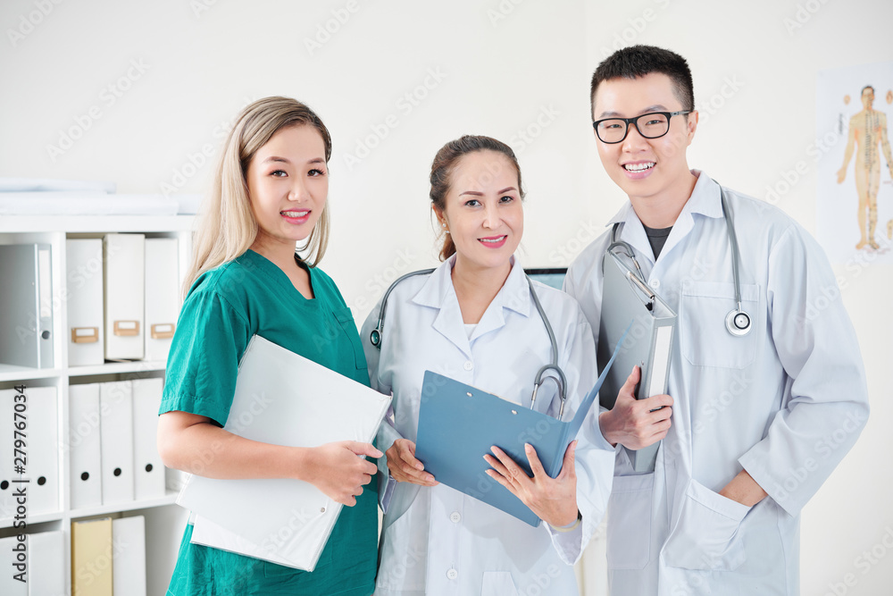 Team of Vietnamese medical workers in scrubs and labcoats posing with document folders
