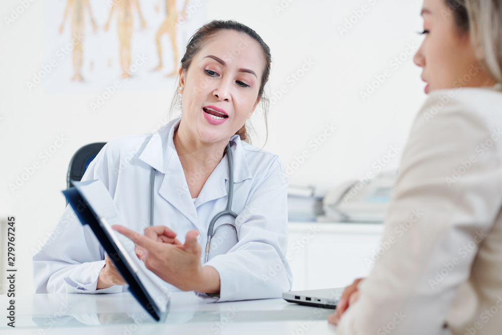 Serious mature experienced cardiologist explaining cardiogram to female patient Serious mature experienced cardiologist explaining cardiogram to female patient