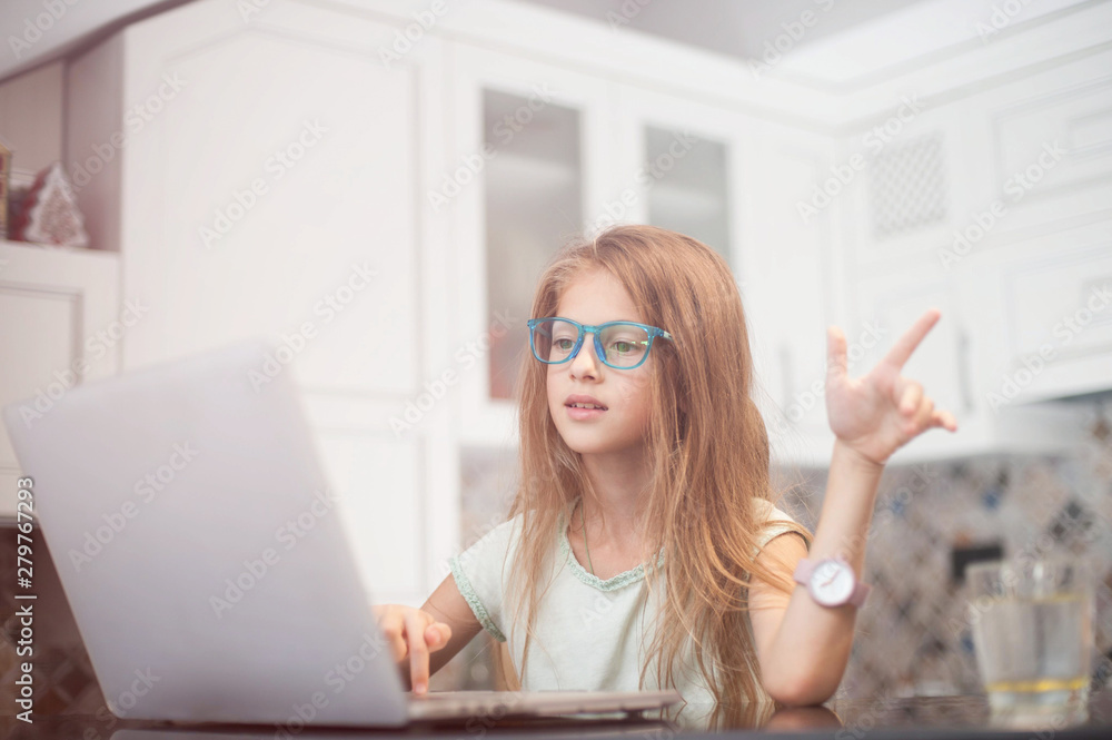 beautiful little girl wearing glasses sitting in home kitchen with laptop online internet chat beautiful little girl wearing glasses sitting in home kitchen with laptop online internet chat