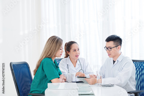 Group of Vietnamese doctors gathered at table to discuss article on new innovative treatment on tablet computer