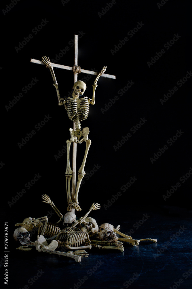 The skeleton on wooden cross and pile of bone on dirty dark floor and black background