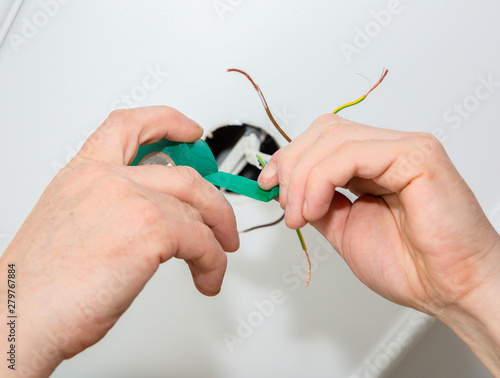 Man is holding adhesive tape in his hands. Electrical insulator for light bulb. Maintenance repair works in the flat. Restoration indoors.