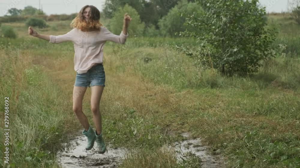 Beautiful smiling teen girl jumping in very muddy puddle on country road, summer nature background after rain Beautiful smiling teen girl jumping in very muddy puddle on country road, summer nature background after rain