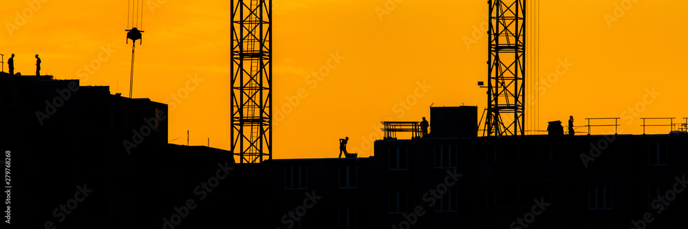 Background of silhouette building crane lift loads with sun set rays yellow cloudy evening sky backdrop Construction site at orange sunset