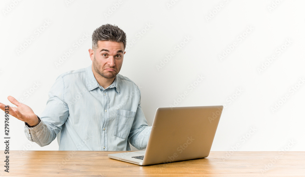 Young handsome man working with his laptop doubting and shrugging shoulders in questioning gesture. Young handsome man working with his laptop doubting and shrugging shoulders in questioning gesture.