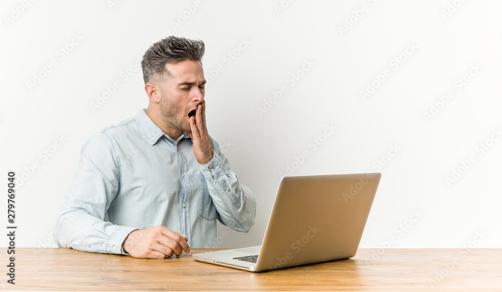Young handsome man working with his laptop yawning showing a tired gesture covering mouth with hand. Young handsome man working with his laptop yawning showing a tired gesture covering mouth with hand.
