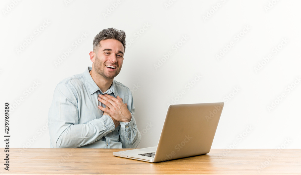 Young handsome man working with his laptop laughing keeping hands on heart, concept of happiness. Young handsome man working with his laptop laughing keeping hands on heart, concept of happiness.