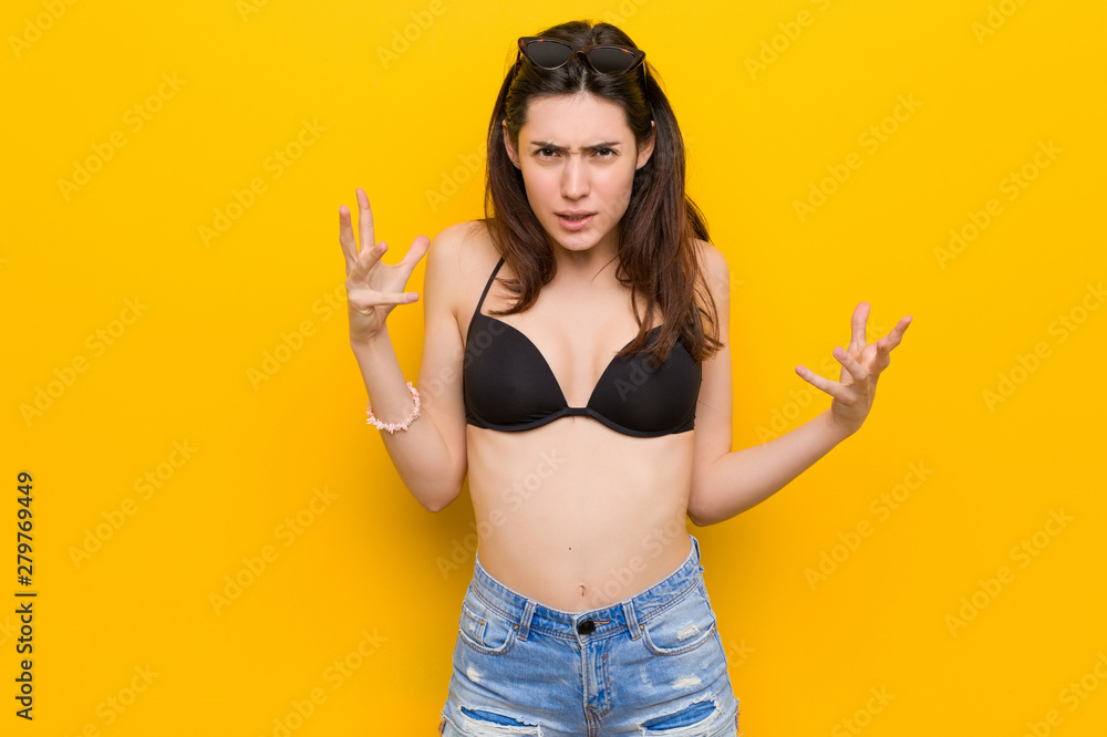 Young brunette woman wearing a bikini against yellow background screaming with rage. Young brunette woman wearing a bikini against yellow background screaming with rage.