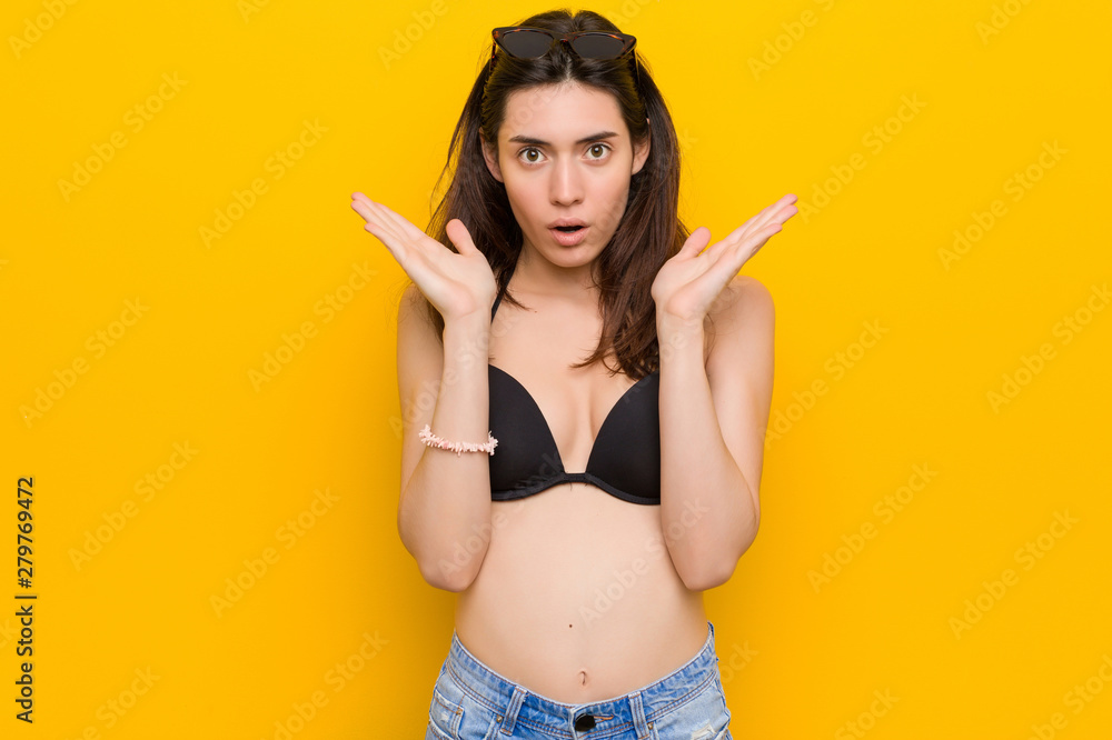 Young brunette woman wearing a bikini against yellow background surprised and shocked. Young brunette woman wearing a bikini against yellow background surprised and shocked.