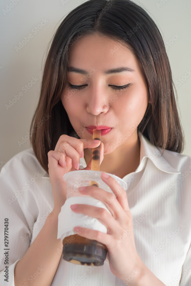 Happy smiling asian woman drinking iced bubble milk tea; aka boba tea, pearl milk tea, tapioca tea, asian exotic beverage concept; retouched image Happy smiling asian woman drinking iced bubble milk tea; aka boba tea, pearl milk tea, tapioca tea, asian exotic beverage concept; retouched image