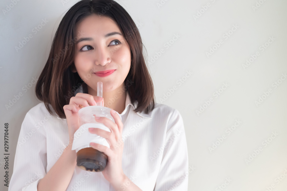 Happy smiling asian woman drinking iced bubble milk tea; aka boba tea, pearl milk tea, tapioca tea, asian exotic beverage concept; retouched image Happy smiling asian woman drinking iced bubble milk tea; aka boba tea, pearl milk tea, tapioca tea, asian exotic beverage concept; retouched image