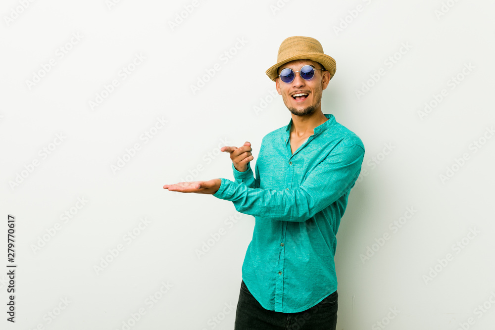 Young hispanic man wearing a summer clothes excited holding a copy space on palm. Young hispanic man wearing a summer clothes excited holding a copy space on palm.