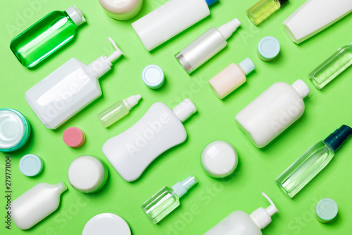 Top view of different cosmetic bottles and container for cosmetics on green background. Flat lay composition with copy space