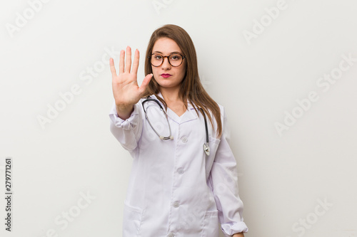 Young doctor woman against a white wall standing with outstretched hand showing stop sign  preventing you.