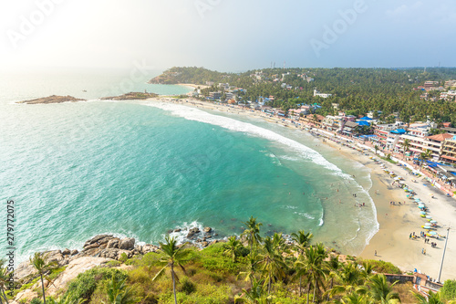 Fototapeta Naklejka Na Ścianę i Meble -  Aerial view of tourists taking a dip in the turquoise waters of Lighthouse beach at Kovalam, Trivandrum. Tropical feel with green coconut trees and blue waters. India
