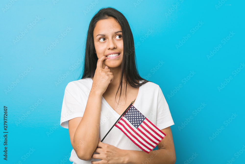 Young hispanic woman holding a united states flag relaxed thinking about something looking at a copy space. Young hispanic woman holding a united states flag relaxed thinking about something looking at a copy space.