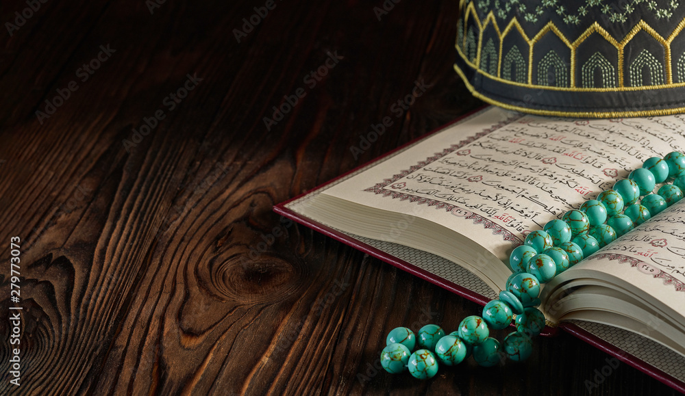 Open Quran book with rosary beads and kopiah hat for muslims on wooden table - obrazy, fototapety, plakaty 