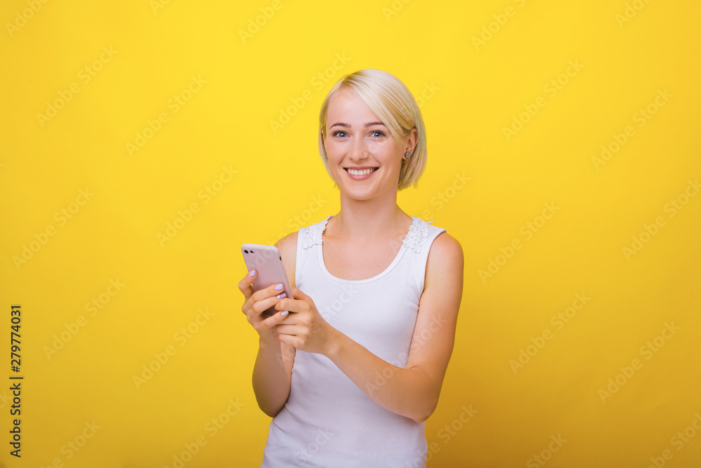 Handsome young blonde woman, lookind at camera while holding a mobile phone Handsome young blonde woman, lookind at camera while holding a mobile phone