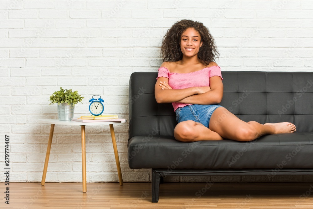 Young african american woman sitting on the sofa who feels confident, crossing arms with determination. Young african american woman sitting on the sofa who feels confident, crossing arms with determination.