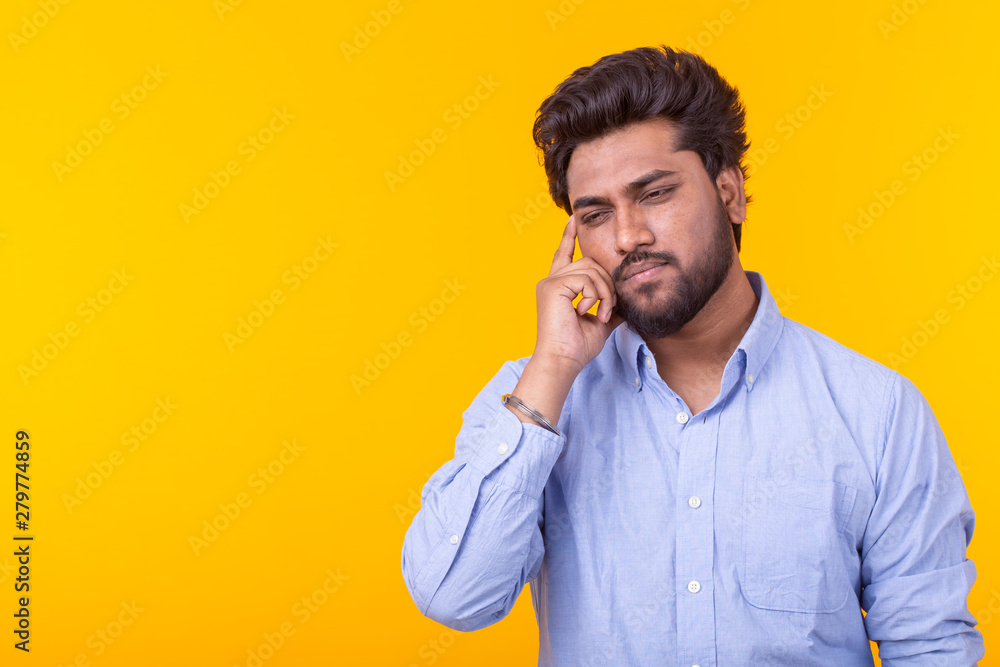 Stylish sad pensive indian young man with a beard in a blue shirt posing on a yellow background. Space for advertising. Concept of thinking. Stylish sad pensive indian young man with a beard in a blue shirt posing on a yellow background. Space for advertising. Concept of thinking.