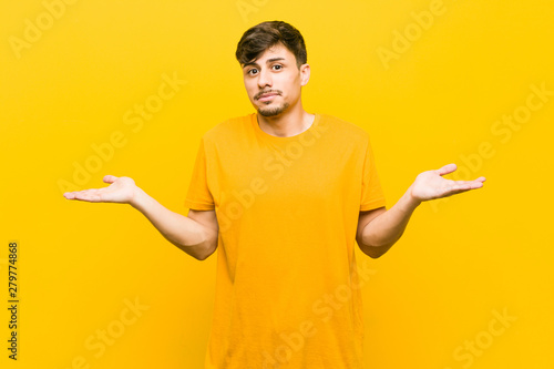 Young hispanic casual man doubting and shrugging shoulders in questioning gesture. photo