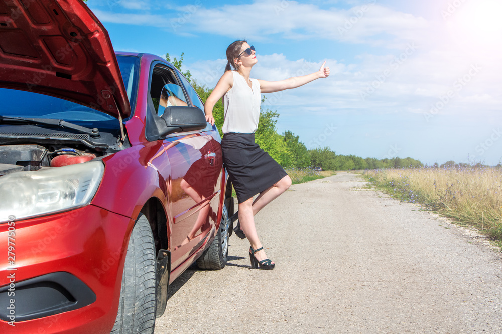 Hitchhiking girl. Beautiful business girl standing near broken car on road and catching a passing car.