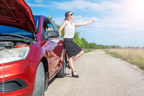 Hitchhiking girl. Beautiful business girl standing near broken car on road and catching a passing car. © Валерий Моисеев