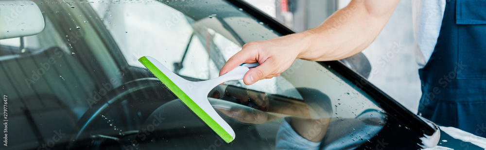 panoramic shot of car washer holding squeegee while cleaning car window
