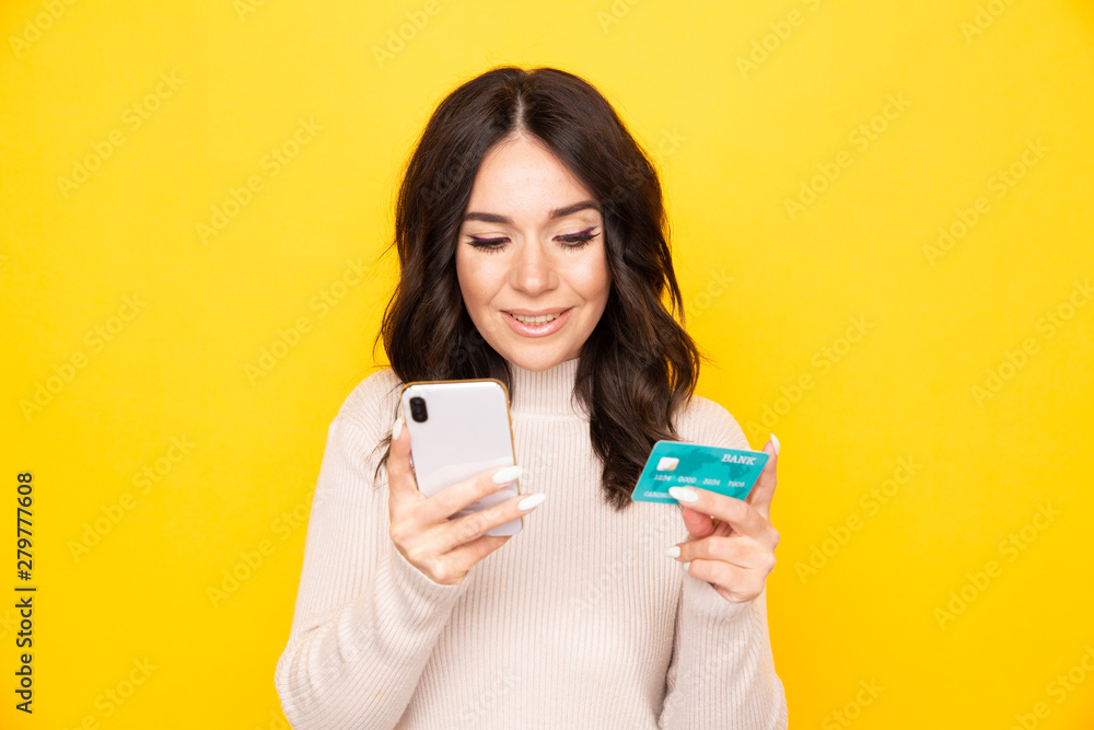 Woman using phone and credit card isolated at the yellow background Woman using phone and credit card isolated at the yellow background