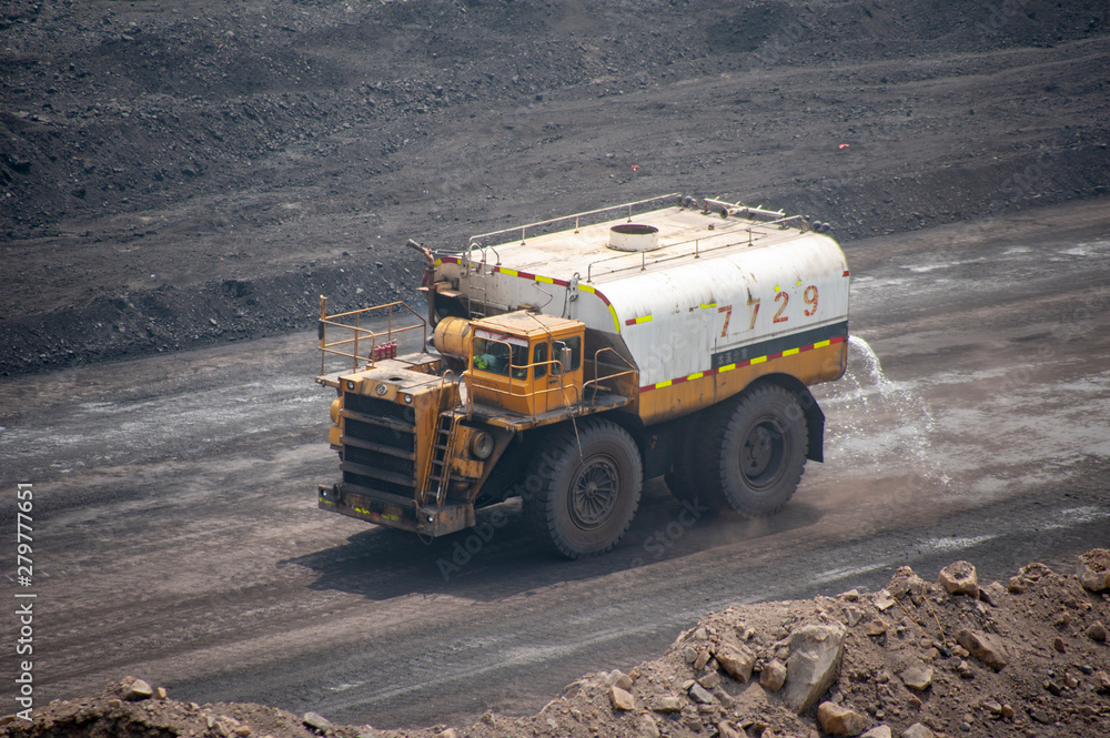 Obraz premium Big yellow truck spraying water in dusty Chinese coal mine