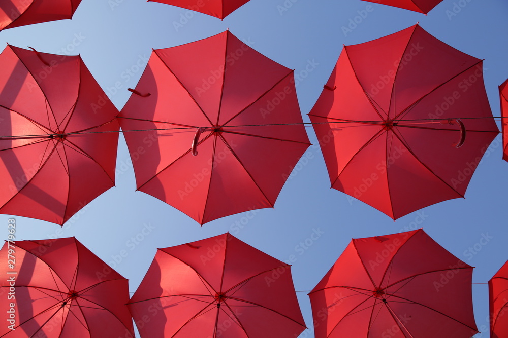Red umbrellas against the blue sky. View from below. Abstract background with red umbrellas. Seamless pattern with umbrellas. Red umbrellas against the blue sky. View from below. Abstract background with red umbrellas. Seamless pattern with umbrellas.