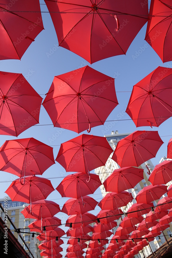 Obraz premium Red umbrellas against the blue sky and the bright building. Abstract background with umbrellas