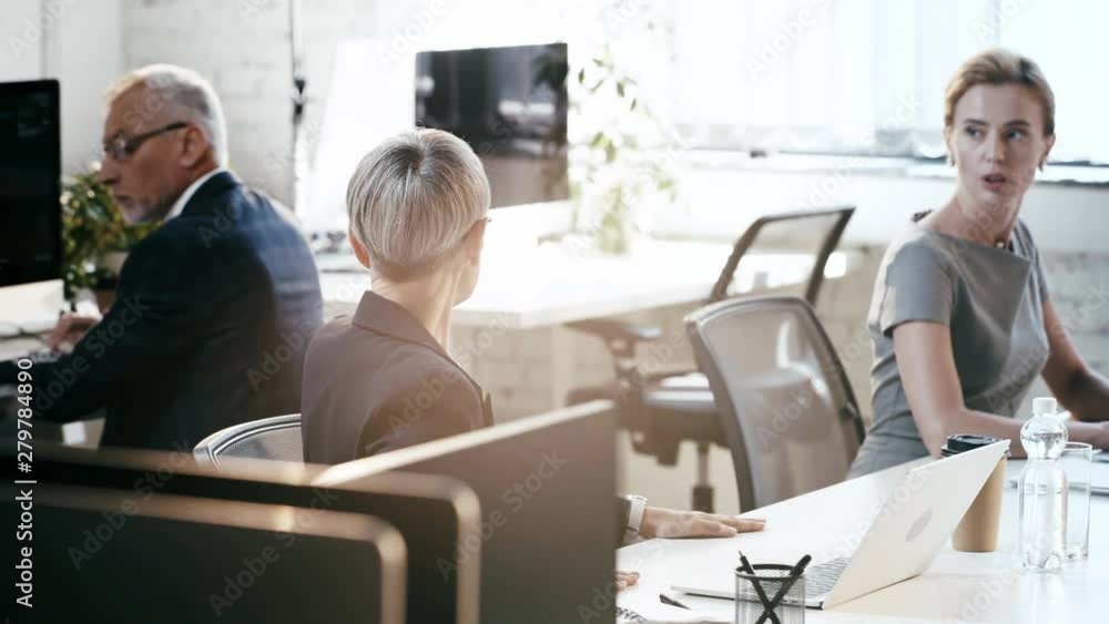 selective focus of businesswoman using laptop, then gesturing and talking near businessman holding contract near colleagues in office selective focus of businesswoman using laptop, then gesturing and talking near businessman holding contract near colleagues in office