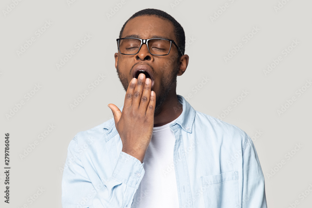 © fizkes - Tired black man feel sleepy cover mouth yawning