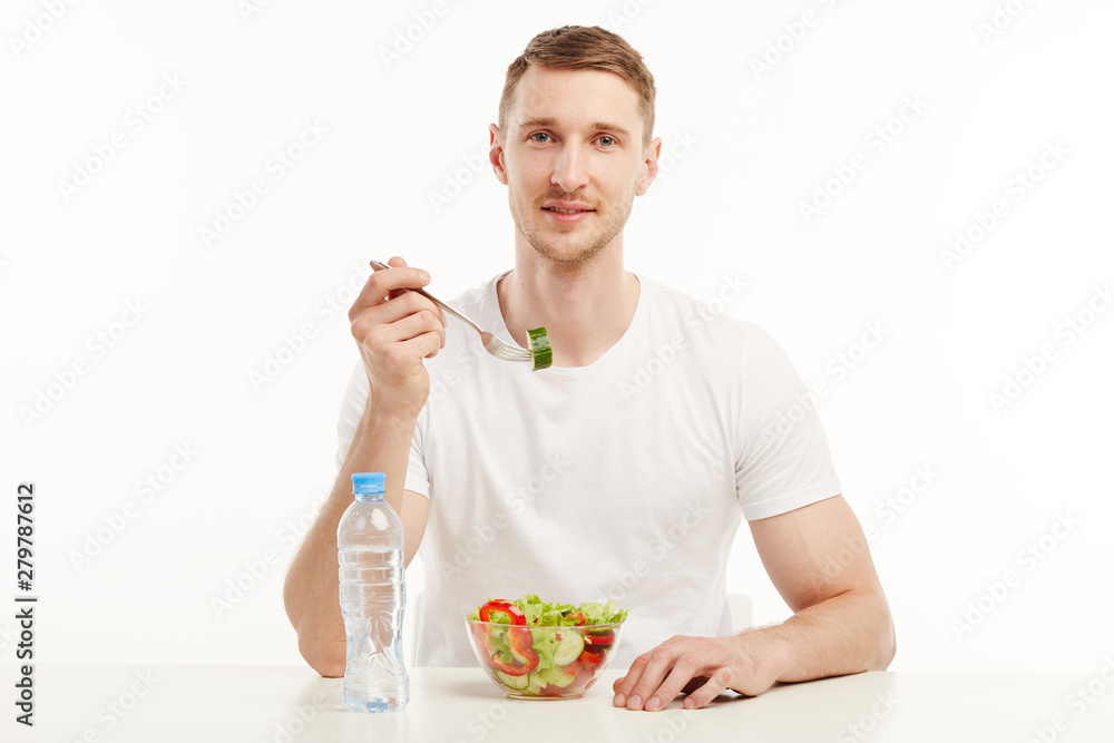 Muscular guy eating vegetable salad from a glass bowl. Muscular guy eating vegetable salad from a glass bowl.