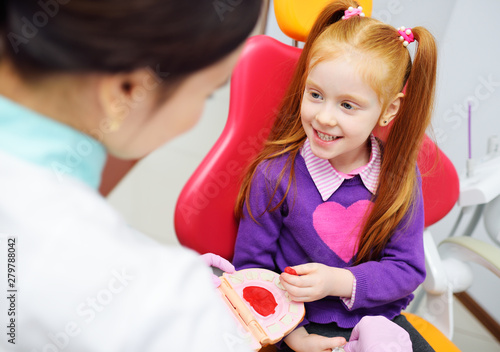 the baby is a little red-haired girl and a female pediatric dentist playing doctor with toy dental instruments sitting in the dental chair.