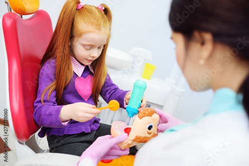 the baby is a little red-haired girl and a female pediatric dentist playing doctor with toy dental instruments sitting in the dental chair.