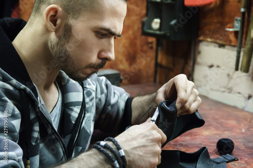 Craftsman intently works with leather. Tanner sews leather goods. Making handmade stuff. Male hands with needle and thread. Man working with needle and pliers. 