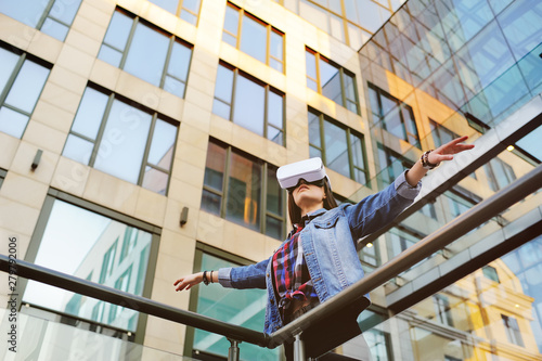 Beautiful girl in denim jacket with long hair playing VR game standing in front of glass building © Evgeniy Kalinovskiy