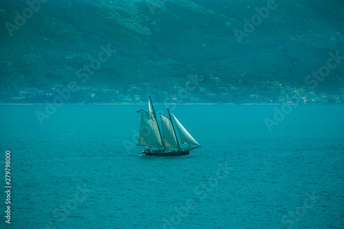 Boat with three sails in vintage retro style on a turquoise background of water and mountains