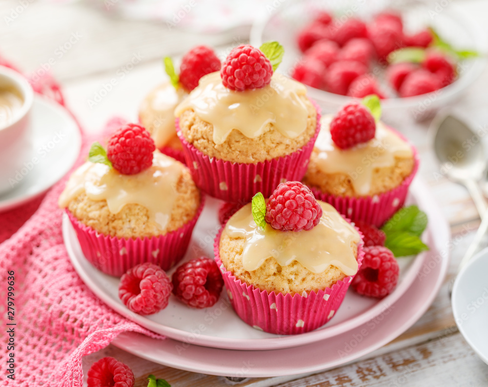 Cupcakes with white chocolate and fresh raspberries on a ceramic plate on a wooden white table.  A delicious dessert or breakfast.