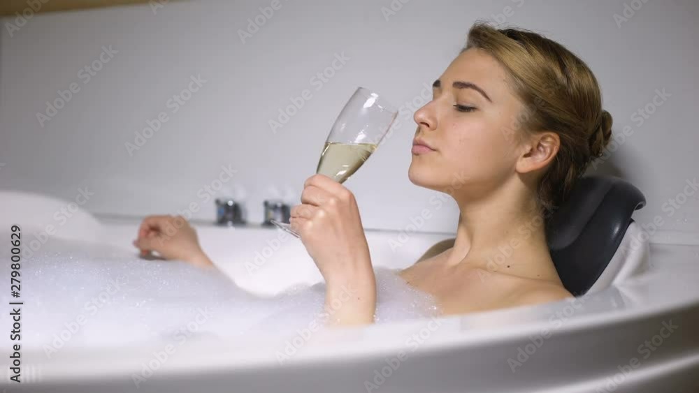 Elegant lady drinking champagne in bath with foam bubbles, chilling and relaxing Elegant lady drinking champagne in bath with foam bubbles, chilling and relaxing