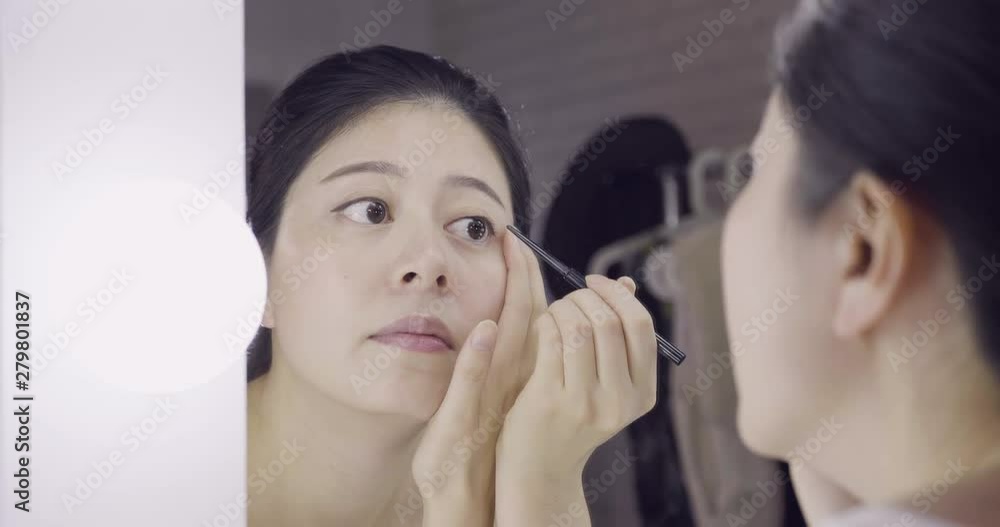 Eyeliner eye makeup beauty care concept. Asian girl artist putting eye liner pencil on eyes looking in mirror at vanity table. asian woman celebrity applying make up in backstage dressing room. Eyeliner eye makeup beauty care concept. Asian girl artist putting eye liner pencil on eyes looking in mirror at vanity table. asian woman celebrity applying make up in backstage dressing room.