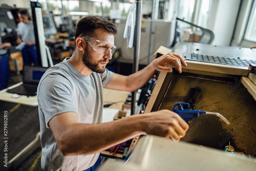 Young worker operating a CNC machine while working in industrial facility. Young worker operating a CNC machine while working in industrial facility.