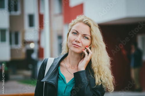 Beautiful blonde girl with curly hair talking on a smartphone on a city street. The work of a freelancer, the decision of working moments.