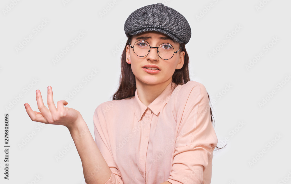 Questioned young woman, looking serious at discussing things, dressed in casual outfit, posing over white wall. Student girl has confused expression. People emotions Questioned young woman, looking serious at discussing things, dressed in casual outfit, posing over white wall. Student girl has confused expression. People emotions