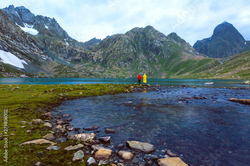Fototapeta Naklejka Na Ścianę i Meble -  Friends fishing at Vishnusar lake on Kashmir great lakes trek in Sonamarg, India. Rocky terrain and  turquoise lake/tarn with snow mountains and glacier. Amazing nature. Hiking Trekking in Himalayas