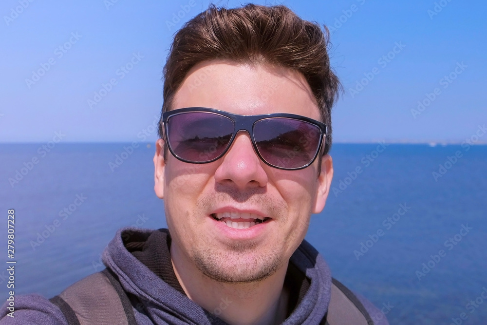 Portrait of young guy on sea background. Man blogger traveller selfie camera talks about vacation at sea. Young tourist smiles and shares his impressions about rest at sea. Travel journey concept. Portrait of young guy on sea background. Man blogger traveller selfie camera talks about vacation at sea. Young tourist smiles and shares his impressions about rest at sea. Travel journey concept.